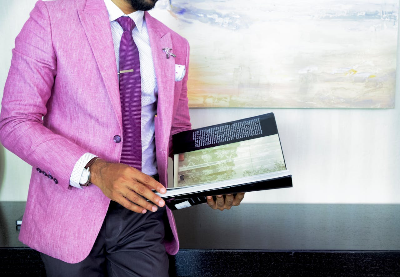 Home A businessman in a pink suit holding a book, symbolizing success and professionalism.