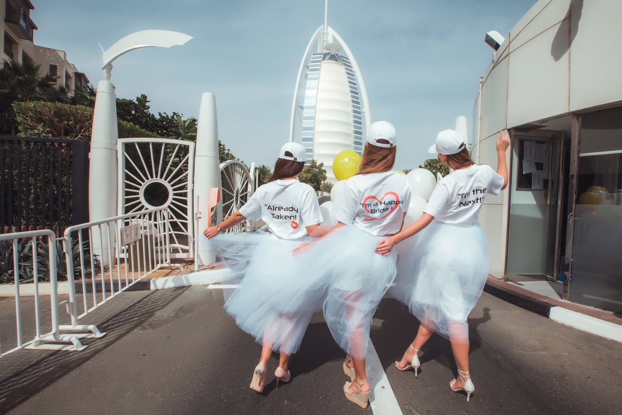 Home Three women in bridal party attire walking towards the Burj Al Arab for a fun hen party celebration.