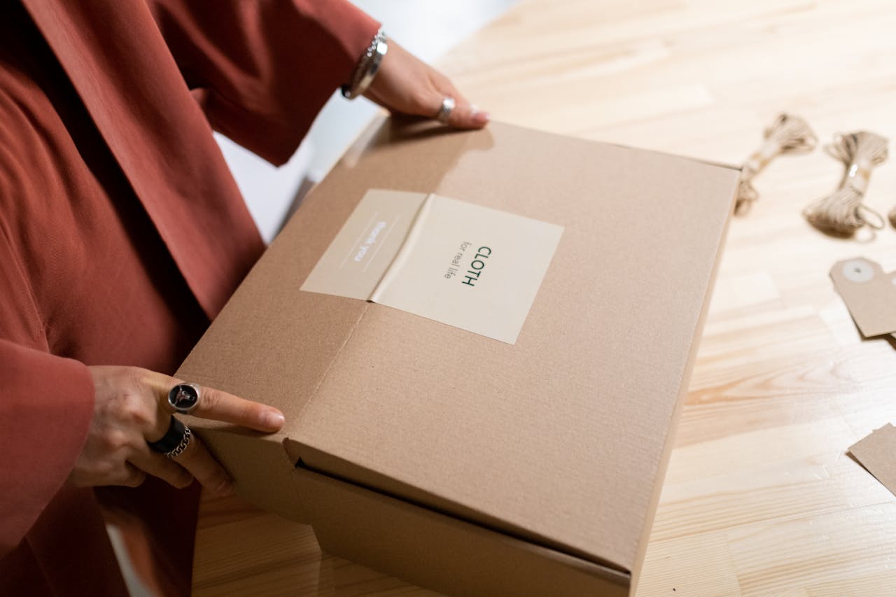 Close-up of a woman packing a cardboard box on a wooden table indoors.